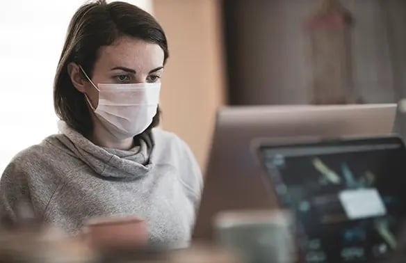 a woman working in her desktop while wearing a mask 
