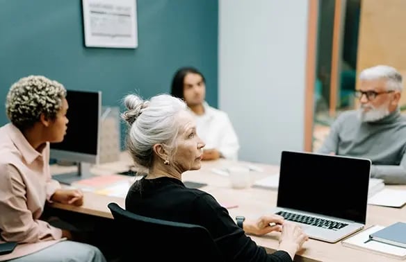 woman in black sweater sitting on a chair in front of a macbook pro